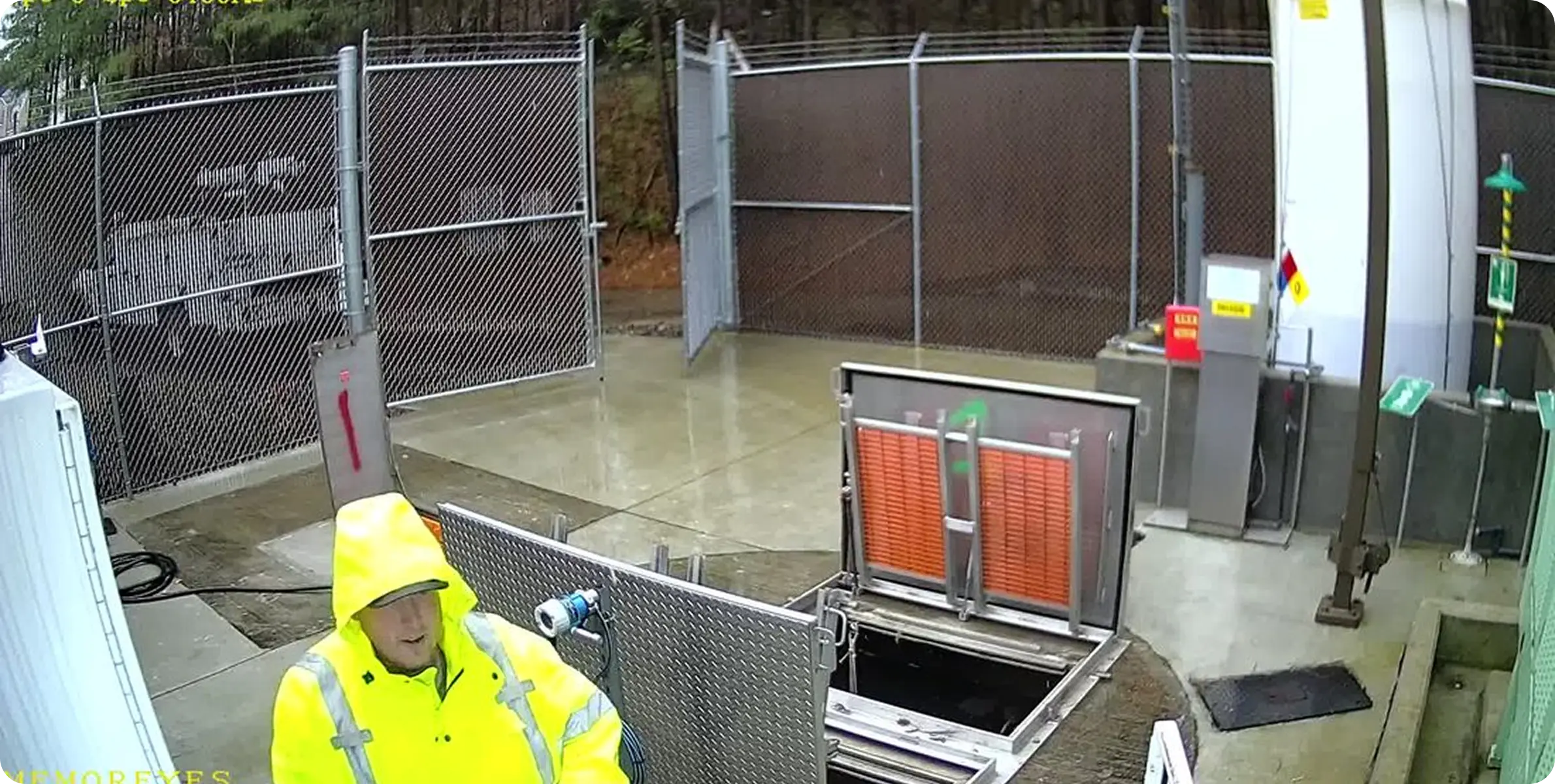 Memoreyes Municipal A man in a yellow raincoat and hat stands in front of a chain-link fence, with a large metal gate behind