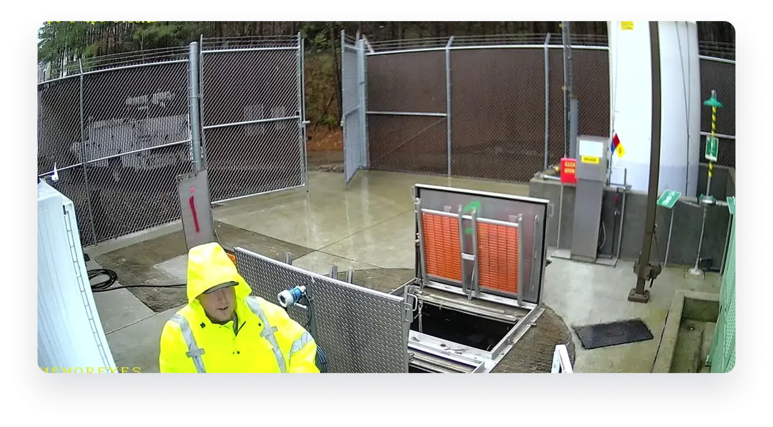 Sentry camera view of an operator in a rain jacket beside an open lift station hatch
